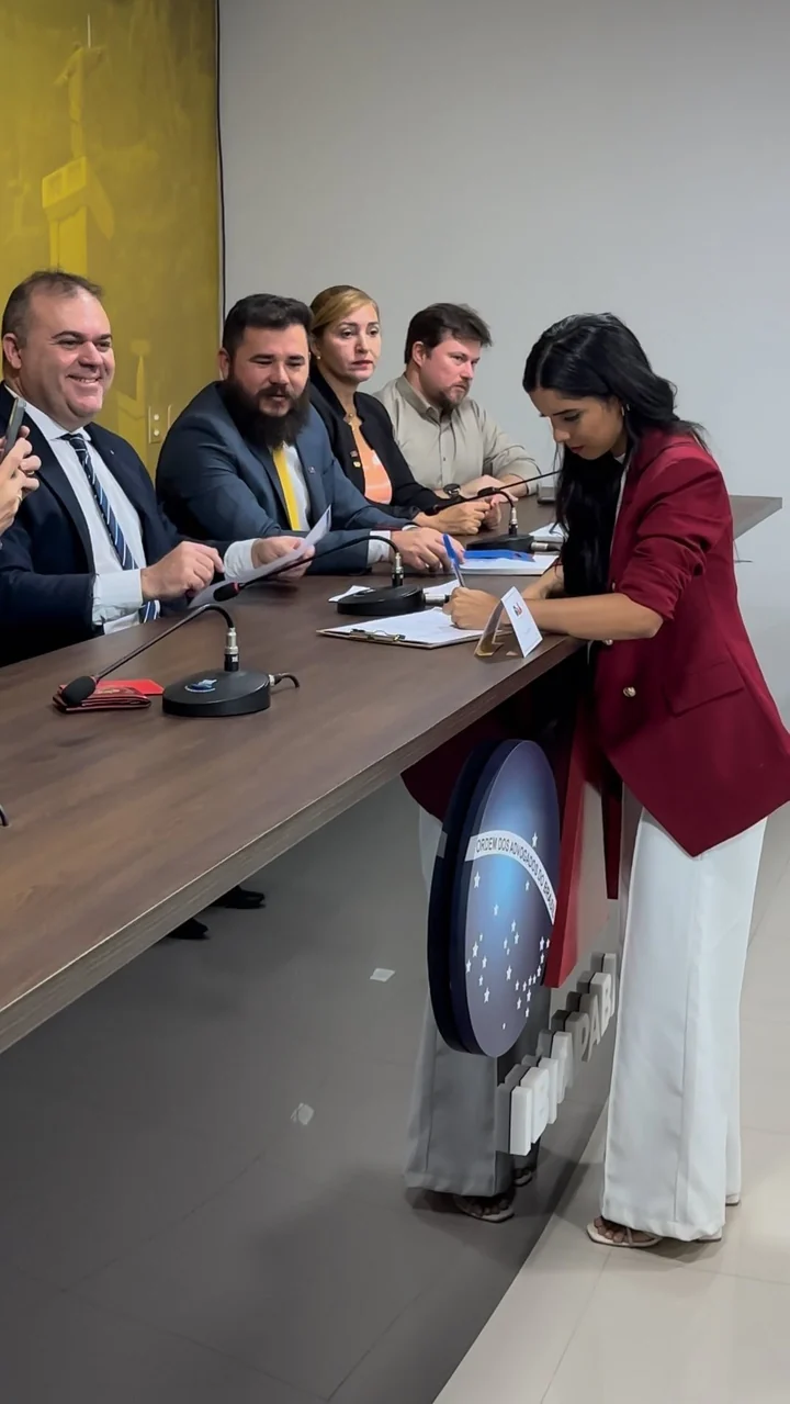 Vanessa Britto assinando um documento em uma cerimônia na OAB